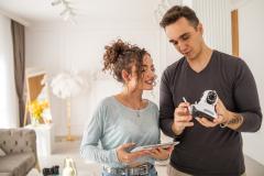 une jeune femme avec un jeune homme qui tient une camera de surveillance pour l'installer dans une maison