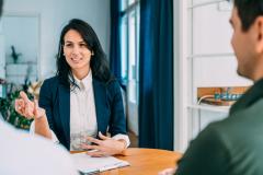 une femme devant un bureau fait face à deux hommes pour signer un docuement