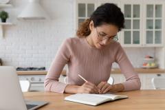 Jeune femme devant son ordi en train de prendre des notes