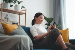 Femme assise sur son canapé en train de regarder son téléphone