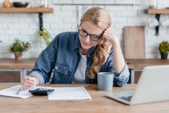 Femme blonde concentrée effectuant des calculs devant son pc, la tête en appui sur son bras