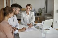 Un couple souriant signe le document que leur présente une femme.