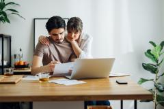 Un couple étudie un document devant un ordinateur, à son domicile. 