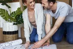 Un couple agenouillé sur le sol échange devant le plan de sa future maison