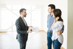 Un professionnel, un rapport à la main, donne des explications à un jeune couple debout face à lui dans un appartement. 