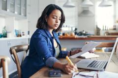 Une femme travaille sur son ordinateur, installée sur la table de sa cuisine