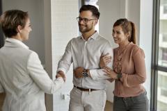 Un jeune couple souriant serre la main d'une femme dans un appartement