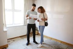 Un couple étudie des documents dans une pièce de son logement nécessitant des travaux de rénovation