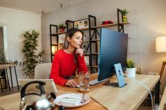 Une femme, installée à un bureau, consulte des documents sur son ordinateur personnel, dans son salon