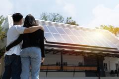 Couple enlacé, debout près de sa maison sur laquelle ont été installés des panneaux photovoltaïques