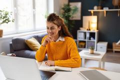 Une femme souriante télétravaille sur une table, dans son salon 