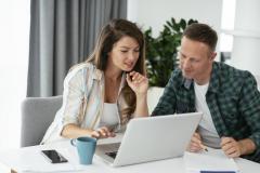 Un couple, installé autour d'une table de salon, étudie un dossier sur son ordinateur