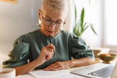 Une femme tente de comprendre un document au format papier, assise devant son ordinateur portable