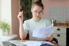 Une chose femme assise à un bureau fait des calculs, en étudiant divers documents au format papier