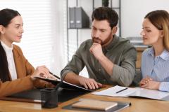 Un couple étudie avec attention un document au format papier présenté par son notaire au cours d'un rendez-vous