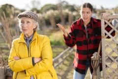 Une jeune femme, appuyée contre la barrière de son terrain, a un différend avec une voisine plus âgée qui s'éloigne en lui tournant le dos