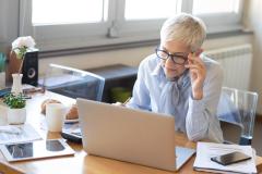 Une femme aux cheveux blancs très courts se charge de dossiers administratifs sur son pc portable
