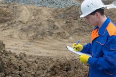 Un ingénieur muni d'un casque de chantier réalise l'étude géotechnique d'un terrain