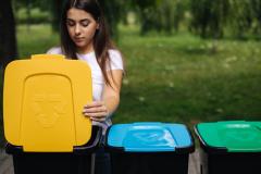 Une jeune femme aux cheveux longs jette un emballage dans le bac de tri jaune