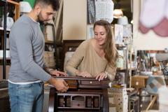 Un jeune couple admire un petit secrétaire ancien en bois dans un magasin d'antiquités