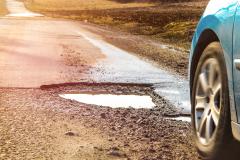 Une voiture emprunte une route endommagée, présentant plusieurs nids-de-poule remplis d'eau