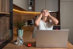 Une jeune femme travaillant sur son pc portable se bouche les oreilles en regardant le plafond de son appartement