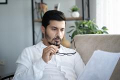 Un homme, lunettes à la main, étudie avec attention un dossier au format papier