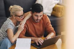 Un couple effectue des recherches sur un ordinateur portable, dans son salon