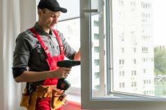 Un artisan, en salopette et casquette, installe un nouveau vitrage sur la fenêtre d'un logement