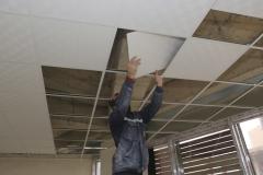 Un ouvrier pose des dalles sur des rails dans le cadre de la réalisation d'un faux-plafond