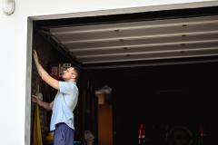 Un homme vérifie une installation dans son garage ; la porte de son garage est ouverte en grand