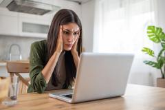 Une femme brune aux cheveux longs se tient la tête dans ses mains devant son pc portable, soucieuse