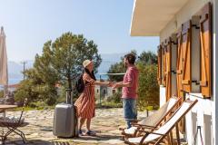Un propriétaire accueille sa locataire, qui arrive avec sa valise pour un séjour de courte durée dans sa maison