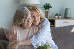 Une femme d'âge mûr serre dans ses bras sa maman âgée, avec un grand sourire et les yeux fermés, pour la remercier