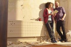 Un couple adossé contre un mur regarde avec satisfaction l'appartement qu'il est en train de rénover