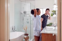 Un homme et une femme en pyjama se sourient devant le miroir de leur magnifique salle de bain