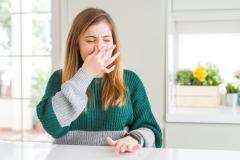 Une jeune femme se bouche le nez, en grimaçant, gênée par une mauvaise odeur