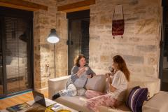 Deux femmes en pyjama discutent dans le salon, confortablement installées sur un canapé placé devant un mur en pierres