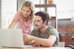 Un jeune couple étudie avec attention des dossiers sur un ordinateur portable