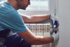 Un chauffagiste en bleu de travail effectue l'entretien d'un radiateur mural