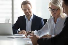 Une femme blonde signe un contrat chez le notaire, avec un grand sourire