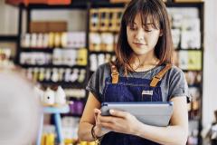 Une jeune entrepreneure portant une salopette en jean travaille à l’aide de sa tablette numérique dans son épicerie fine