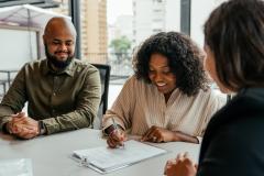 Un couple signe un contrat avec une jeune femme qui représente le promoteur immobilier en charge de la construction de leur maison