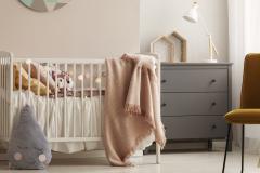 Une chambre d'enfant dans les tons roses avec un lit de bébé et une commode grise