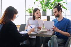 Un jeune couple étudie des documents au cours d'un rendez-vous avec une professionnelle de l'immobilier
