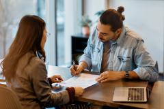 Un jeune homme d'origine hispanique signe un contrat de location dans une agence