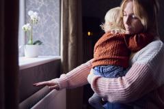 Une maman tenant son bébé dans les bras passe la main au-dessus du chauffage mural pour voir s'il fonctionne