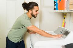 Un jeune homme d'origine hispanique programme son lave-linge dans sa buanderie
