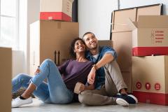 Un jeune couple est assis par terre enlacé, en admirant son nouveau logement rempli de cartons de déménagement
