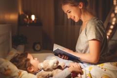 Une maman, assise sur le lit de son petit garçon, lui lit une histoire avant qu'il s'endorme